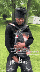 a man wearing a black hat and holding a backpack is standing in a grassy field .