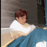 a man with red hair is laying on a bed with a blue blanket and a white shirt .