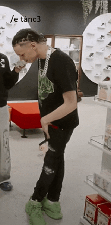 a man in a black shirt and green shoes is standing in a store with a / e tanc3 watermark