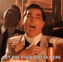 a man in a suit and tie is holding a glass of wine and yelling .