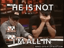 a man is sitting at a poker table with his hands folded and another man is sitting behind him .