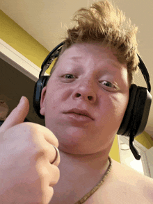 a shirtless young man wearing headphones giving a thumbs up