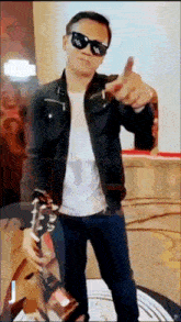 a man wearing sunglasses is holding a guitar and pointing to the camera
