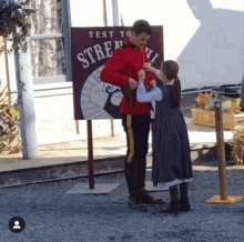 a man in a red uniform is standing next to a little girl in front of a sign that says test your stre