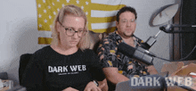 a man and a woman are sitting in front of a microphone and a sign that says dark web