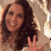 a woman with curly hair giving a peace sign and smiling
