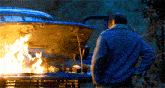 a man stands in front of a burning car