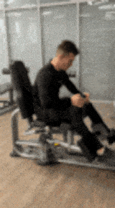 a man is sitting on a machine in a gym and looking at his phone .