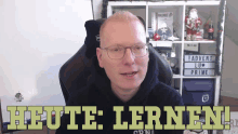 a man wearing glasses sits in front of a sign that says i advent lu prime