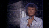 a man singing into a microphone with a brick wall behind him