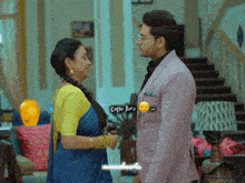 a man in a pink suit and a woman in a blue sari are standing next to each other and the man says come here