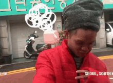 a man in a red jacket is standing in front of a sign that says " seoul south korea "