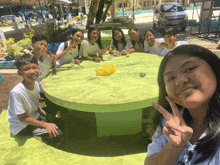 a group of young people are sitting around a green table and one girl is giving a peace sign