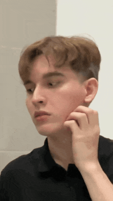 a young man in a black shirt is looking at his face in the mirror .