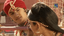 a man in a red turban is touching a woman 's forehead with a sony television logo in the corner