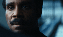 a man with a mustache is looking at the camera in a dark room