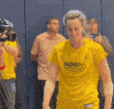 a woman wearing a yellow indiana basketball t-shirt is standing in front of a camera .