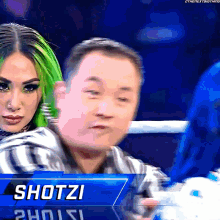 a woman with green hair stands next to a referee with the name shotzi on it