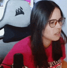 a woman wearing glasses and a red shirt is sitting in front of a corsair chair .