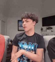 a young man with curly hair is sitting in a chair wearing a black t-shirt with the word ohio on it .