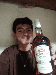 a young man is holding a bottle of alfonso light whiskey