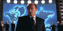 a man in a suit and tie is standing in front of a large screen with a map of the world on it .
