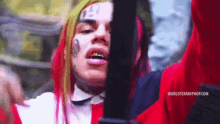 a man with red hair and a tattoo on his face is holding a gun in his hand .