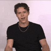 a young man with curly hair wearing a black t-shirt and a silver chain around his neck