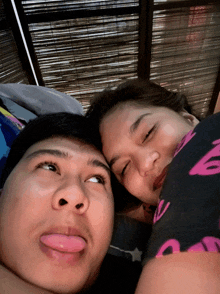 a man sticking his tongue out while laying next to a woman wearing a shirt that says a