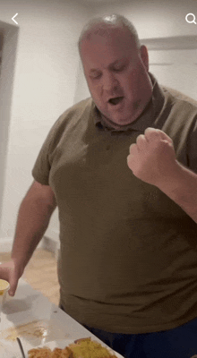 a man in a green shirt is standing in front of a plate of food with a fist in the air