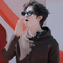 a young man wearing sunglasses and a hoodie shouts