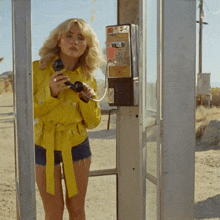 a woman in a yellow jacket talks on a payphone