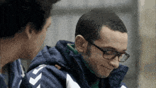 a man wearing glasses and a blue jacket with a white arrow on it