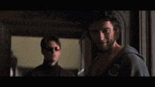 a man wearing sunglasses stands next to another man wearing a shirt that says ' x-men ' on it