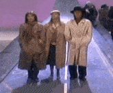 a group of people in trench coats and hats are standing next to each other on a runway .