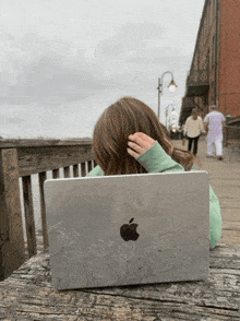a woman is sitting on a wooden bench with an apple laptop