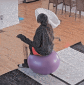 a woman sits on a purple exercise ball in a living room