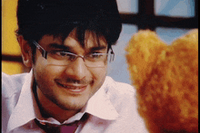 a man wearing glasses and a tie smiles at a teddy bear
