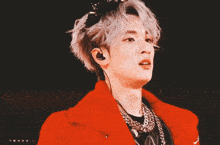 a close up of a person wearing a red coat and necklaces