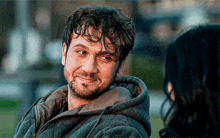 a man with a beard wearing a hoodie looks at a woman