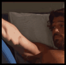 a man with a beard is laying in bed with a blue pillow
