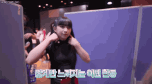 a girl in a black top is standing in front of a blue wall with korean writing on it