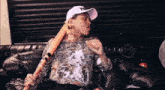 a man is sitting on a couch holding a bat and talking .