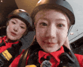 a woman wearing a helmet is standing next to another woman wearing a red jacket