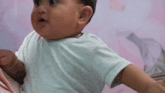 a baby is sitting on a bed with his arms outstretched and looking at the camera .