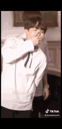 a man in a white shirt and tie is covering his mouth with his hands