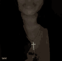 a woman is wearing a necklace with a cross pendant on her neck .