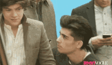 harry styles and zayn malik are sitting next to each other in front of a blue background .