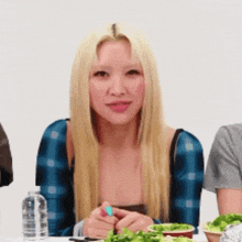 a woman with blonde hair is sitting at a table with a salad and a bottle of water .