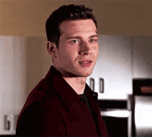 a man in a red shirt and black shirt is standing in a kitchen .